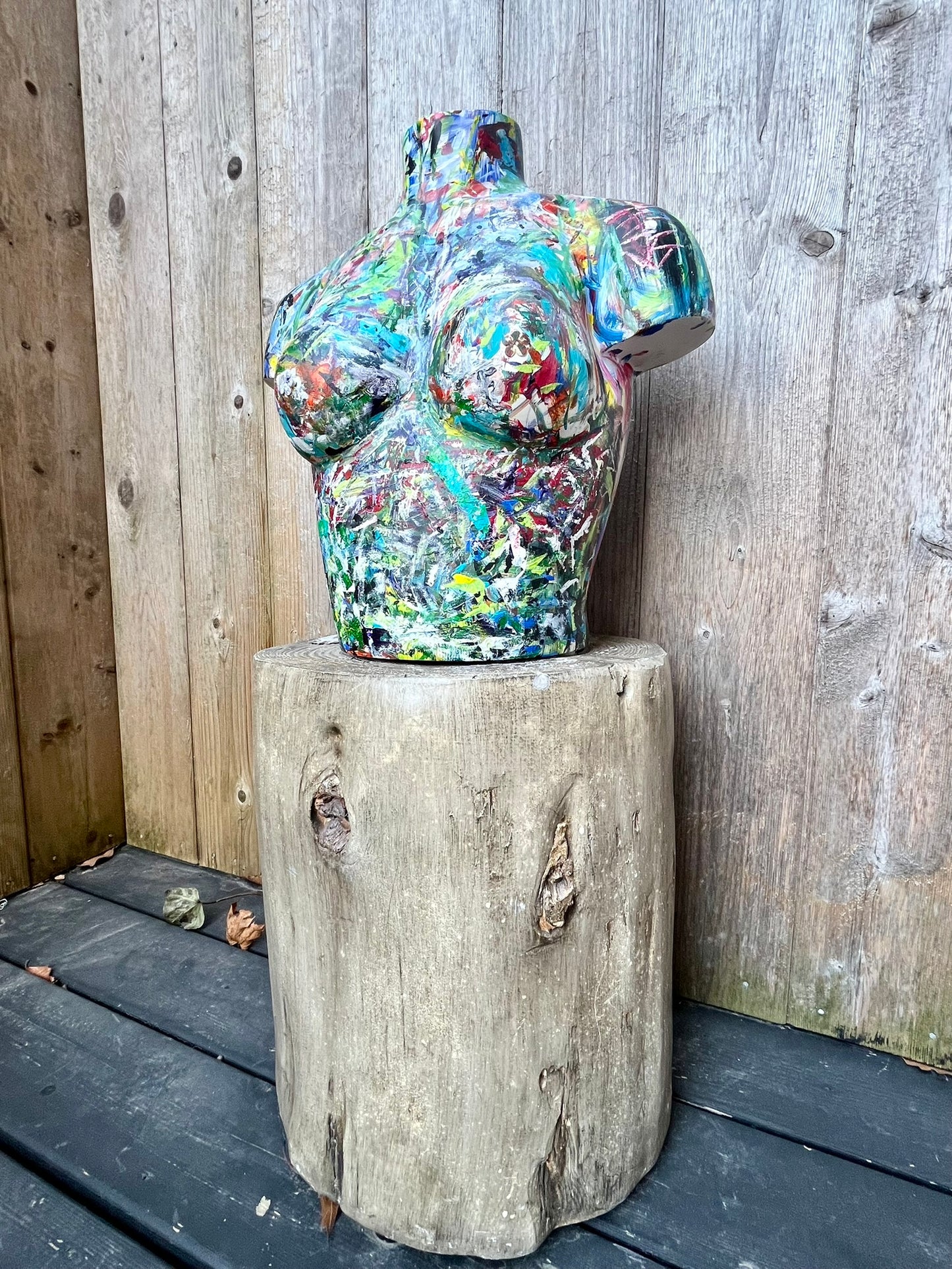 Colorful abstract-painted female torso sculpture by Cindy Trestman, crafted on wood and displayed on a rustic tree stump base.